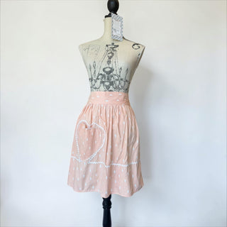 Her Good Eye pink cotton apron with white raindrop pattern and heart pocket with lace trim.