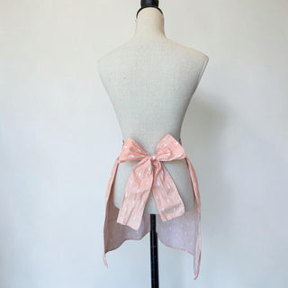 Her Good Eye pink cotton apron with white raindrop pattern and lace-trimmed heart pocket. Ties in a bow.