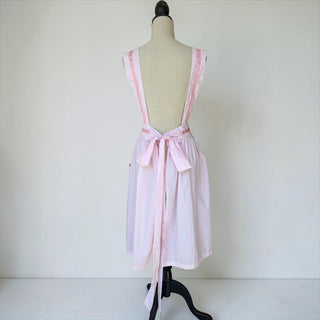 Her Good Eye light pink cotton blend pinafore apron with ribbon trim, adjustable straps, tie waist, and pockets.