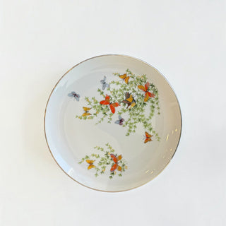 Her Good Eye white porcelain plate featuring colorful hand-painted butterflies and green botanical motifs with a silver rim