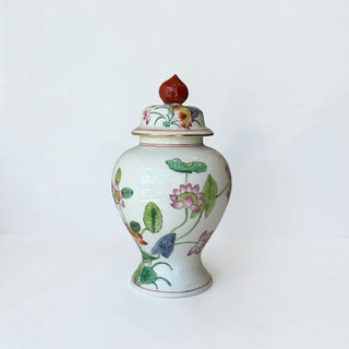 Her Good Eye porcelain temple jar with hand-painted lotus flowers, green foliage, and a bold red finial on the lid.