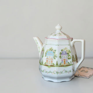 Her Good Eye porcelain teapot featuring a whimsical village house motif with pastel illustrations and scalloped edges.
