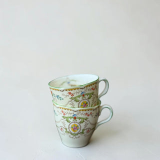 Her Good Eye decorative porcelain teacup with handle, featuring a floral and scrollwork pattern in pastel colors with gold trim.