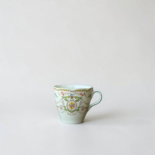Her Good Eye decorative porcelain teacup with intricate floral pattern, gold trim, and curved handle.