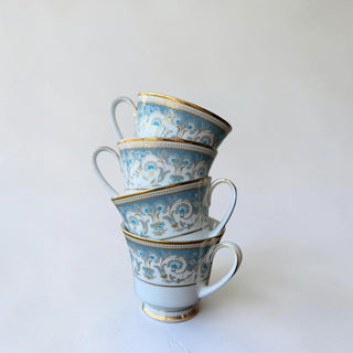 Set of four Her Good Eye decorative porcelain teacups with blue and gold damask pattern and gold rims.