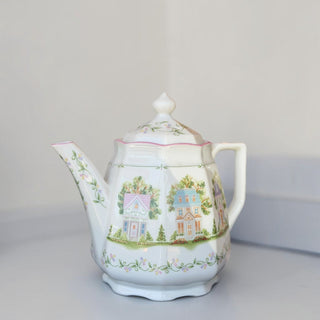 Her Good Eye porcelain teapot featuring a whimsical village house motif with pastel floral accents and scalloped edges.