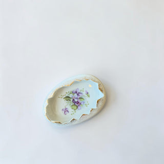 Her Good Eye decorative porcelain trinket dish shaped like an egg with purple floral design and gold trim.