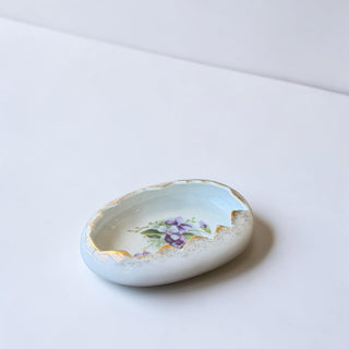 Her Good Eye decorative porcelain trinket dish shaped like an egg with purple floral design and gold trim.