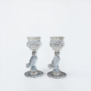 Her Good Eye pair of vintage clear pressed glass candle holders featuring a bird motif and intricate starburst patterns.