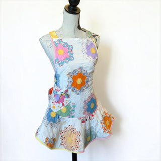 Her Good Eye vintage quilted hexagon patchwork apron with floral motifs, ruffled hem, and side pocket on a mannequin.