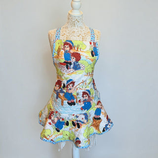 Her Good Eye quilted kitchen apron featuring a vintage Raggedy Ann and Andy print with blue floral trim and front pocket.