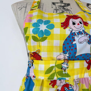 Her Good Eye yellow gingham Raggedy Ann & Andy apron with floral accents and a pocket. Adjustable halter neck and waist ties.