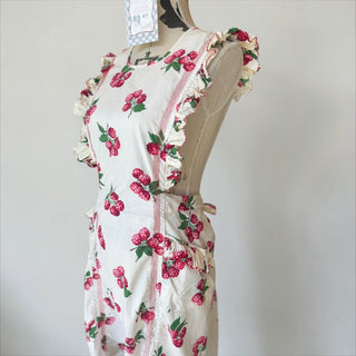 Her Good Eye white cotton apron with raspberry print, ruffled straps, and red pinstripe trim on pockets.