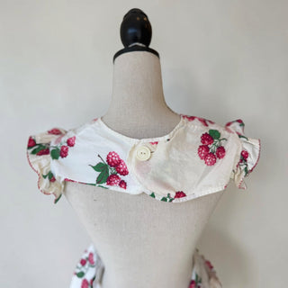 Her Good Eye white cotton apron with raspberry print, ruffles, and red/white pinstripe trim. Features two pockets.