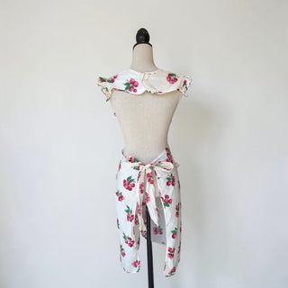 Her Good Eye white cotton apron with all-over raspberry print and ruffled trim. Features tie waist and pockets.