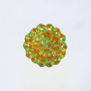 Her Good Eye round crochet coaster in orange, lime green, and white with a scalloped edge and intricate stitch detail.