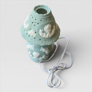 Her Good Eye sage green ceramic table lamp with white neoclassical relief cameos, floral patterns, and heart cutouts.