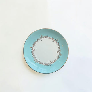 Her Good Eye decorative ceramic dinner plate in sky blue with white center and metallic floral scrollwork accents.