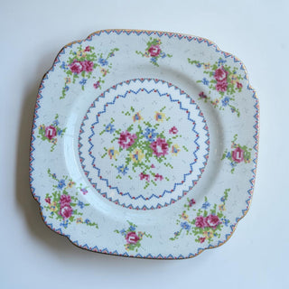 Her Good Eye square dessert plate with floral cross-stitch pattern, gold trim, and scalloped edges.
