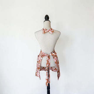Her Good Eye strawberry print cotton apron with matching bow tie, featuring adjustable straps and pockets. White background.