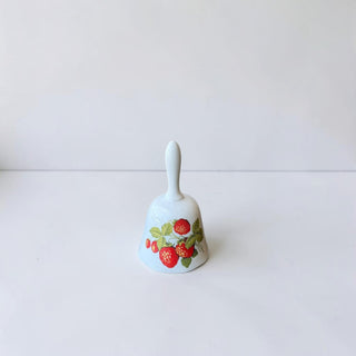 Her Good Eye white ceramic bell with a red strawberry pattern and green leaves. Features a glossy finish and a classic bell shape.