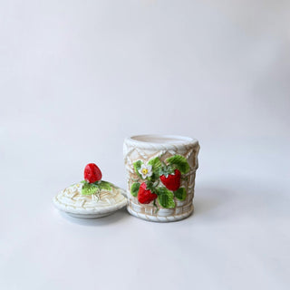 Her Good Eye strawberry ceramic jar with lid, featuring embossed basketweave design, red strawberries, green leaves, and white blossoms.