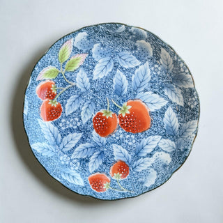 Her Good Eye decorative ceramic plate with a blue background, white speckles, and a strawberry and leaf motif. Scalloped edge with gold trim.