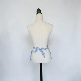 Her Good Eye blue and white striped waist apron tied on a mannequin, showing the back view with adjustable ties.