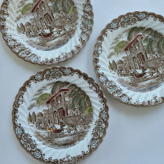 Her Good Eye Victorian era decorative plate with horse-drawn carriages, colonial house, palm trees, and floral border. Sepia tone.