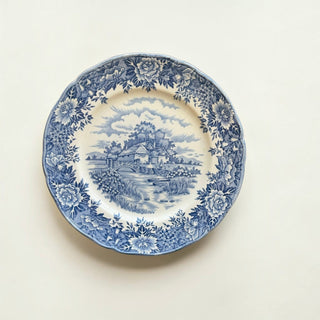 Her Good Eye vintage ceramic dinner plate with blue and white pastoral transferware pattern and scalloped edges.