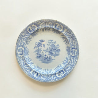 Her Good Eye vintage blue and white porcelain dinner plate featuring a detailed pastoral river landscape scene.