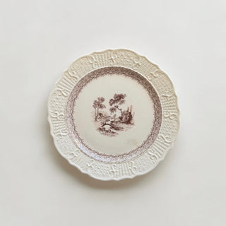 Her Good Eye cream ceramic dinner plate with brown pastoral scene, scalloped edges, and embossed basket-weave detail.