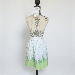 Her Good Eye vintage style cotton waist apron in white with green leaf print and lime green hem on a mannequin.