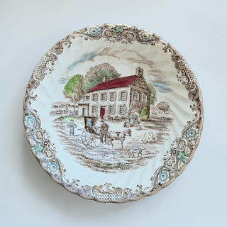 Her Good Eye vintage decorative plate with a sepia-toned pastoral scene, colonial house, horse carriage, and scalloped floral border.