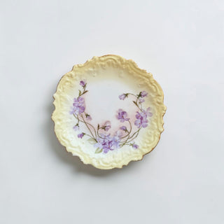 Her Good Eye vintage porcelain plate with purple violet floral pattern, scalloped gold-rimmed edge, and yellow base.