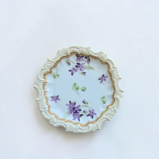 Her Good Eye vintage porcelain plate with hand-painted violet flowers, scalloped relief border, and gold-toned rim.