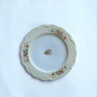 Her Good Eye vintage porcelain dinner plate with cream base, pastel floral motif, and embossed scalloped edges.