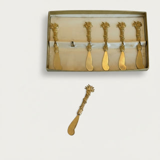 Her Good Eye set of six vintage-style gold-tone metal butter spreaders with textured wheat-inspired handles in a box.