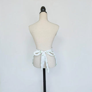 Her Good Eye vintage style white cotton waist apron with green leaf print tied in a bow on a mannequin