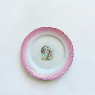 Her Good Eye vintage porcelain display plate with a pink border, embossed scrollwork, and a hand-painted couple scene.