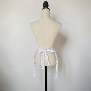 Her Good Eye white cotton half apron with red embroidery on hem and pocket. Adjustable ties.