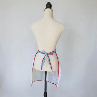 Her Good Eye white linen half apron with blue gingham waistband, red trim, and heart-shaped pocket. Lightweight and sheer.