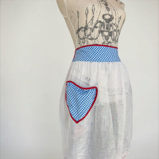Her Good Eye white linen half apron with blue gingham waistband, heart pocket, and red trim. Lightweight and sheer.